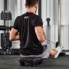 A man is seated on an ATX® Seated Row Seat in a gym, pulling cables. Hes wearing a black T-shirt, gray shorts, and white sneakers, with fitness equipment and weights visible in the background.