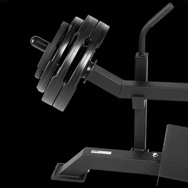 A close-up of a black leg press machine loaded with large weight plates stands against a dark background. Nearby, the ATX Seated Calf Raise Machine is partially visible, showcasing the gym's robust equipment selection.
