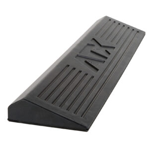 A black, rectangular rubber wheel chock, resembling a squat ramp, with angled sides and grooves on the surface, designed to prevent vehicles from rolling.