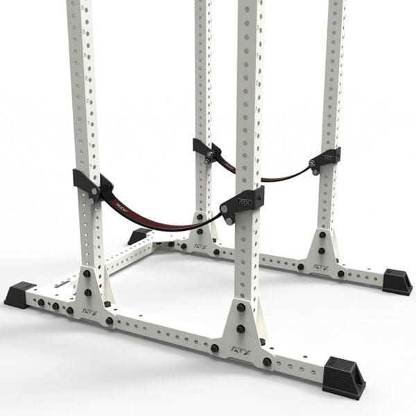 The ATX® Safety Strap System is a white metal squat rack with black foot stabilizers, adjustable safety straps, multiple adjustment holes, and the ATX logo on both the frame and straps, all set against a white background.