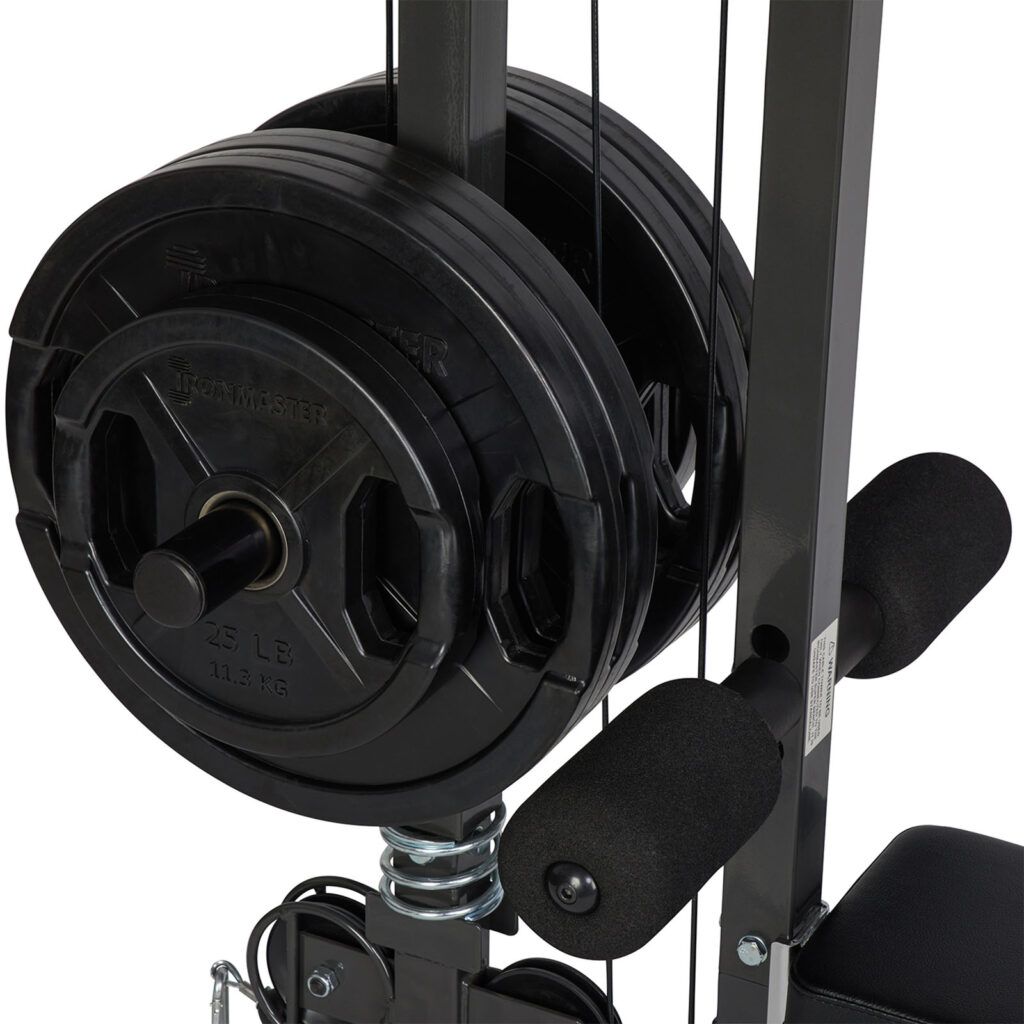 Close-up of the Ironmaster Cable Tower Attachment V2, showcasing multiple black weight plates with a 25 lb mark stacked on a rod. The machine has padded grips and a sleek metal frame.