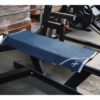 In a fitness center, a Sting Microfibre Gym Towel in blue is neatly placed on a black weight bench. Weight plates and a barbell can be seen behind the bench. The towel features a small logo in one corner.