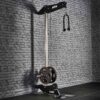 The ATX® Wall Mounted Lat Pulldown boasts a sleek black metal frame, weight plates, and a double-handle grip. It is ideally positioned against a textured gray brick wall in a gym setting, providing both functionality and style for an intense workout experience.