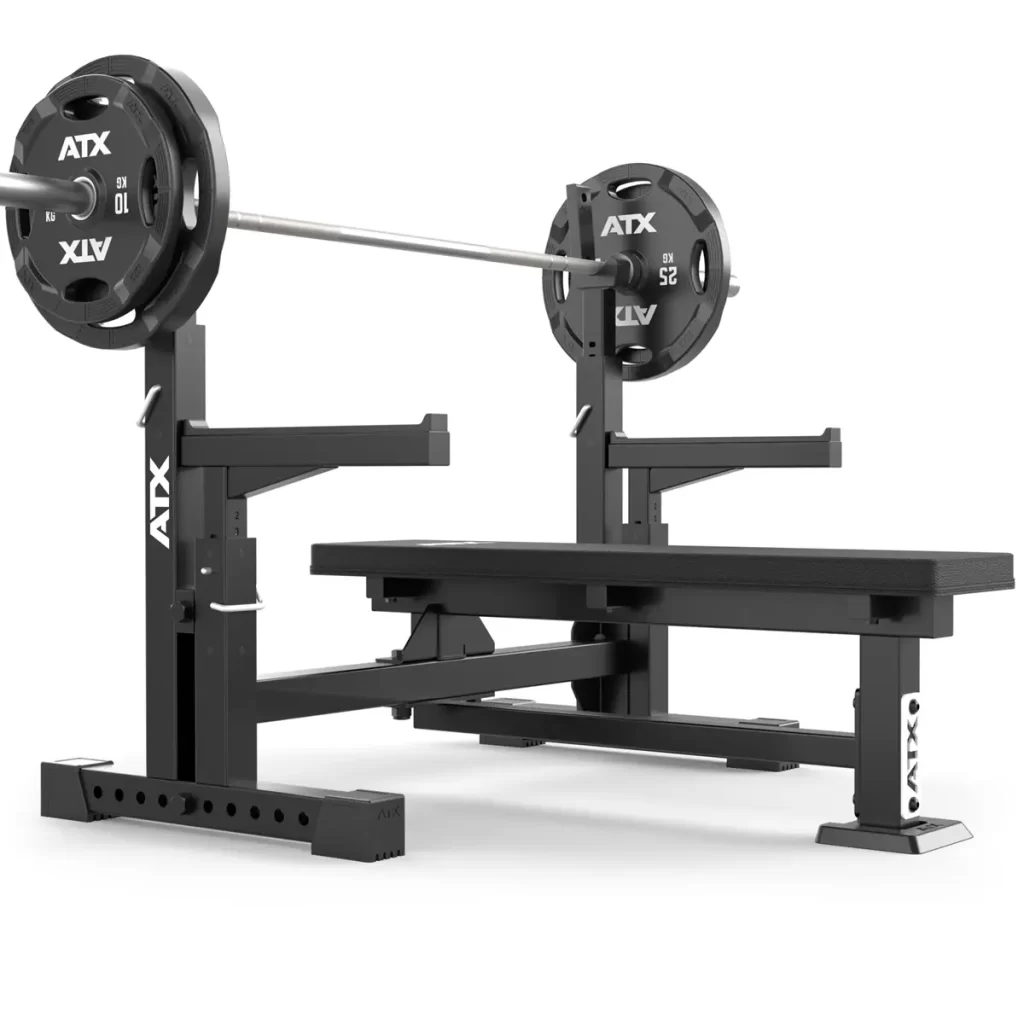 The ATX® Olympic Bench Press 700 features a black and silver sturdy bench with an adjustable metal barbell support. Weighted plates, showing the ATX logo, are attached to the bar on a white background.