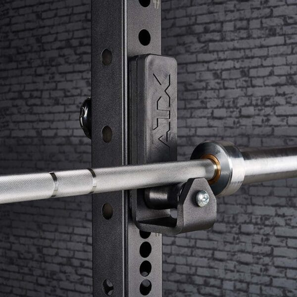 Close-up of an ATX® Roller J-Hooks Universal barbell on a black rack with adjustable holes and ATX branding, set against a textured gray brick wall.