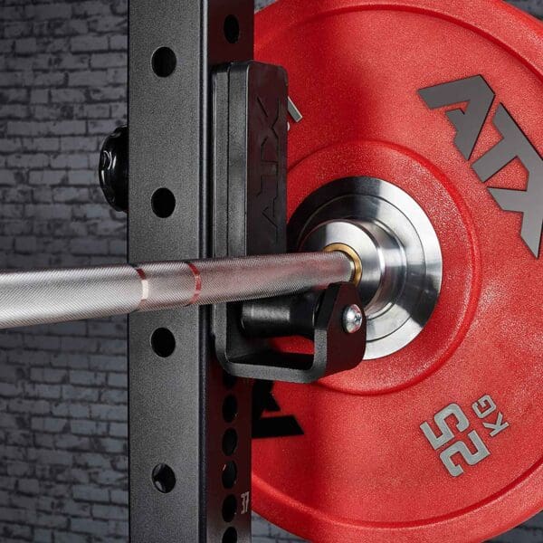 A close-up of a red 25 kg ATX weight plate on a barbell in black ATX® Roller J-Hooks Universal, featuring a textured metal grip with a brick wall backdrop.