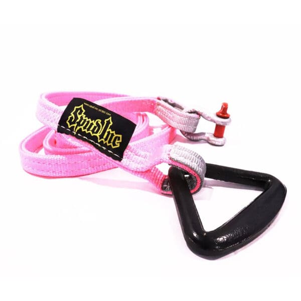 The Spud Inc Sled Attachment Strap PINK features a black triangle-shaped buckle, a black patch with yellow text, and a small metallic red accent on one end.