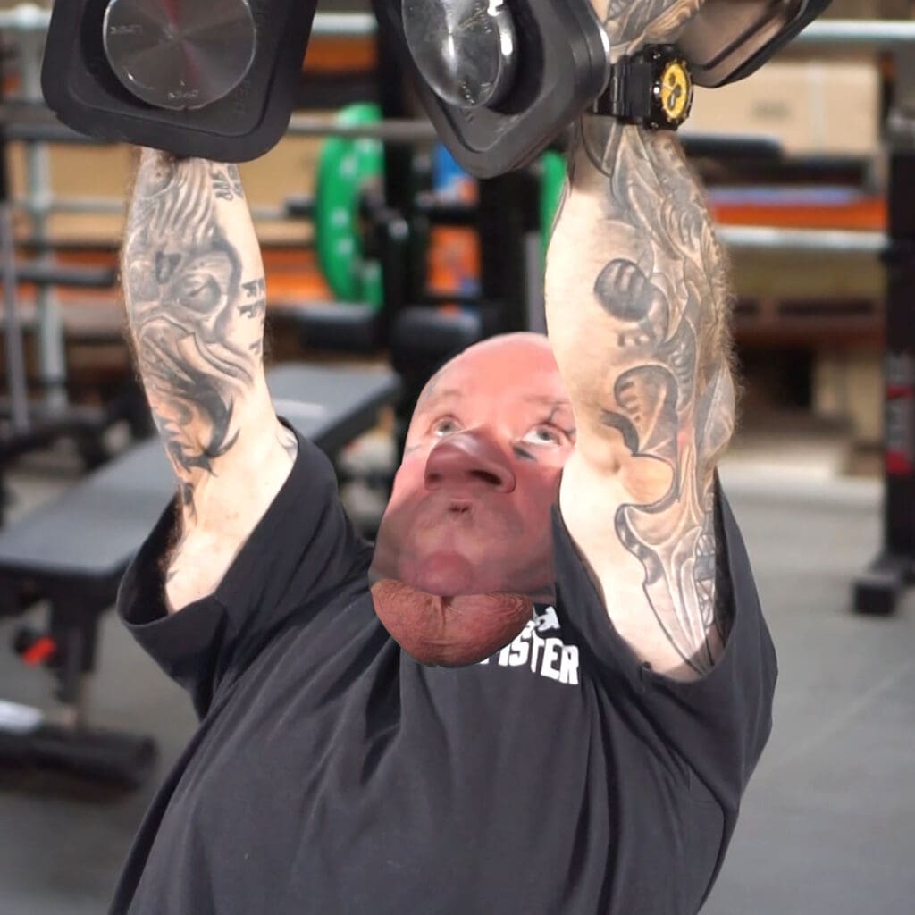 A person with tattooed arms is lying on a bench in a gym, performing dumbbell pec flys. The image is distorted, with the persons head and chin appearing unnaturally enlarged. Gym equipment can be seen in the background.