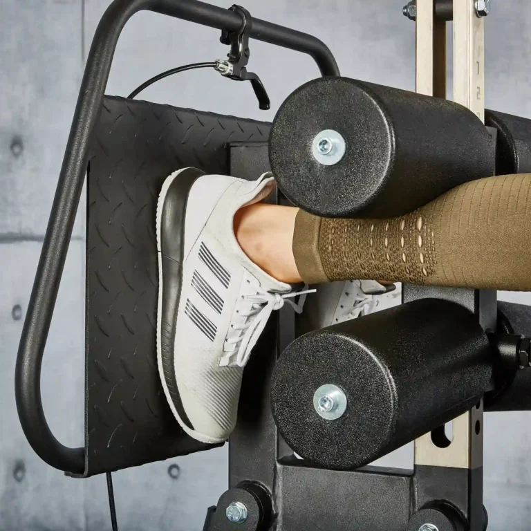 Close-up of a person using a leg press at the gym, seamlessly integrating their workout with a glute and ham raise machine. The focus is on their right foot in a white sneaker with three black stripes, poised on the footplate, complemented by padded rollers supporting their leg.