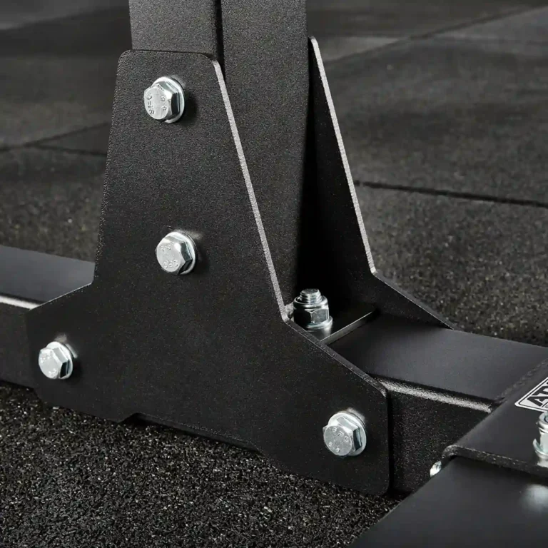 Close-up of a sturdy metal stand with bolts and a black matte finish, resting on a textured rubber floor. This component is part of the ghd gym machine, boasting a strong, angular design that highlights its durability and industrial aesthetic.