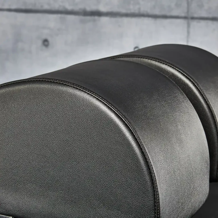 Close-up of a black leather upholstered headrest on a glute and ham raise machine against a gray concrete wall. The design features smooth, rounded shapes with visible stitching, creating a sleek and modern appearance.