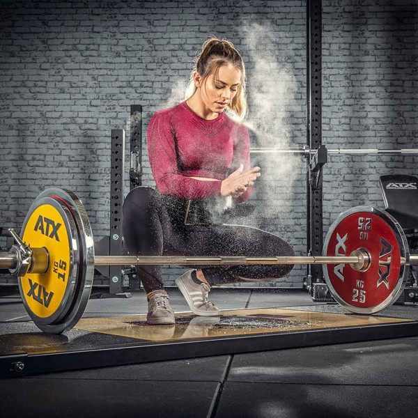 Woman chalking up her hands on a platform with weight and barbells