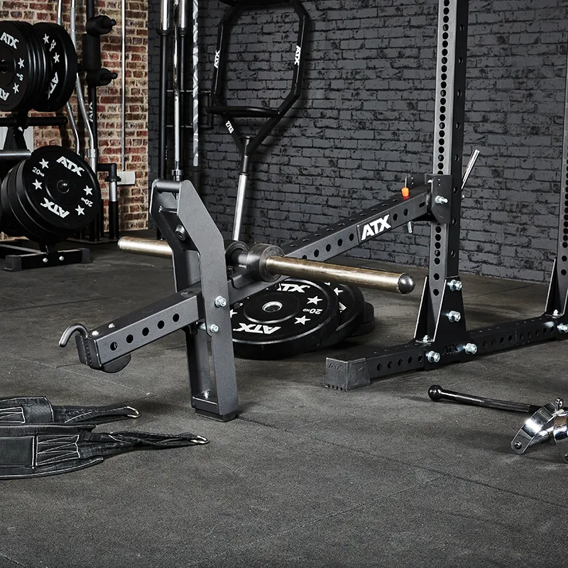 A gym with an ATX® Belt Squat Option, barbell loaded with weights, cable attachments, lifting belts, and extra weight plates against a brick and gray wall.