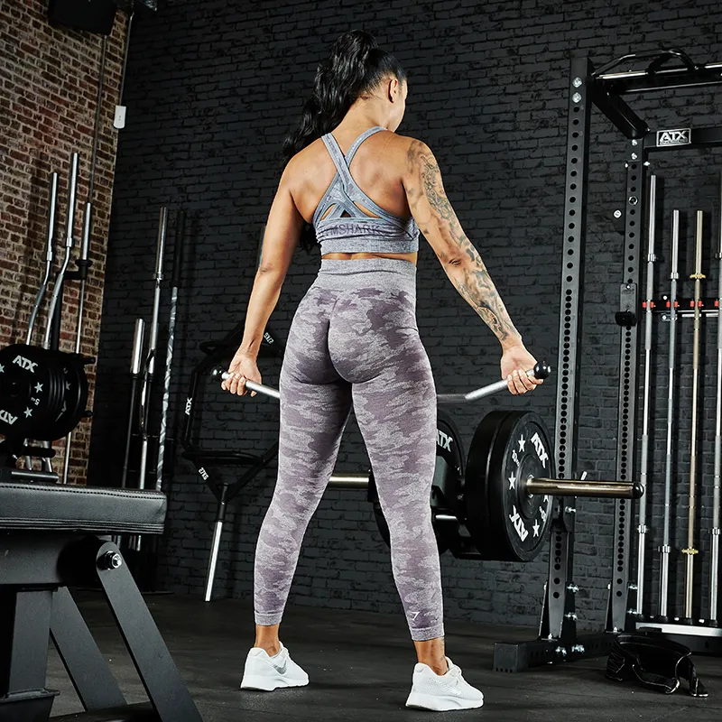 A woman in athletic wear prepares to lift weights with the ATX® Belt Squat Option in a gym, surrounded by equipment and weights, facing away from the camera.