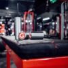 Close-up of two metallic GymPin 2 Original scent diffusers with red logo caps on a gym bench, set against gym equipment and blurred lights, creating a modern, energetic atmosphere.