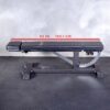 A black Ironmaster Head Extension SB adjustable gym bench sits on a black rubber floor against a gray wall, featuring a 52-inch (132.1 cm) measurement line on its frame.