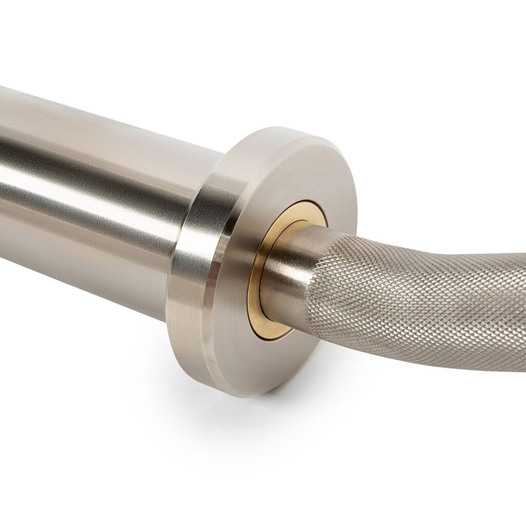 Close-up of the ATX® PRO Ez Curl Bar showcasing its textured, knurled grip section transitioning to a smooth, cylindrical end. The bar boasts a shiny metallic finish accented by a brass-colored ring at the connection point.