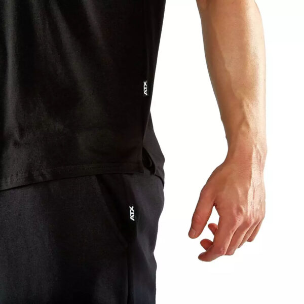 A close-up features someone in the ATX® Training Shirt BLACK and matching pants, showcasing a small ATX logo on both. Their arm is seen against a plain white background.