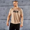 A man in a beige T-shirt with ATX printed on it stands against a concrete wall. He is looking to the side and wearing black athletic pants.