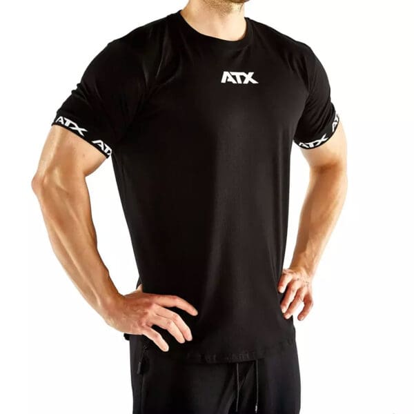 A man confidently poses with hands on hips, wearing a black ATX® Training Shirt featuring ATX on the chest and sleeves, set against a white background.