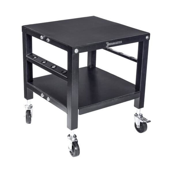 The Ironmaster QLDB Stand PRO is a sturdy black equipment cart with a square design, featuring a flat top surface for adjustable dumbbells, a lower shelf, four swivel casters for easy mobility, and a side rack for accessory storage.