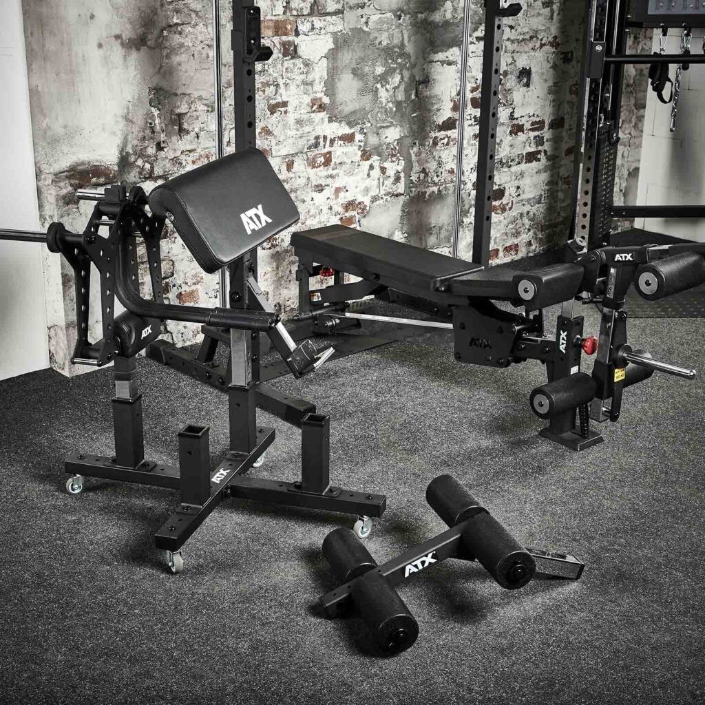 A gym setup features ATX-branded fitness equipment, including an ATX® Attachment Storage Rack, a weight bench, hyperextension bench, and push-up bars on a carpeted floor. The walls showcase a rustic exposed brick design.