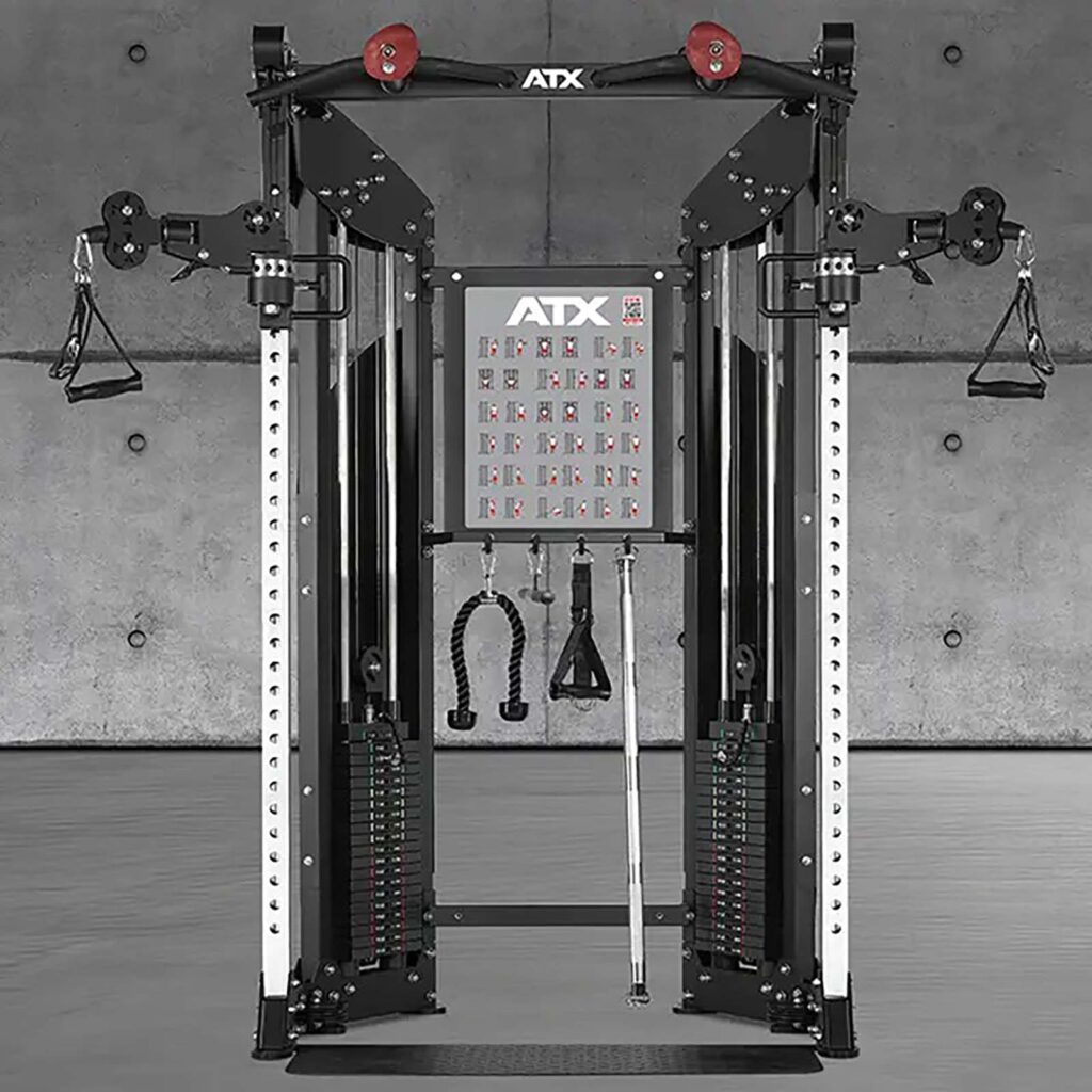 A dual cable crossover machine in a gym setting with adjustable pulleys, weight stacks, and various attachments. The background features a plain concrete wall.
