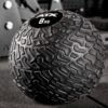Close-up of an ATX® Slam Ball 8 kg featuring a textured surface for grip, resting on a gym mat with blurred fitness equipment in the background.