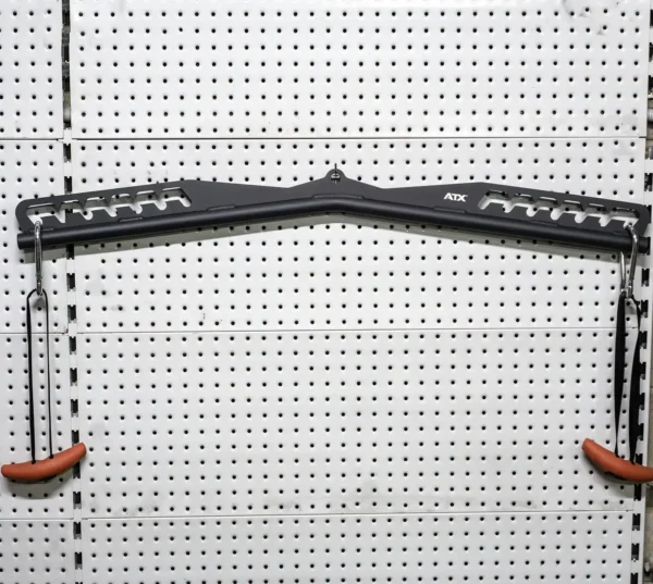 The ATX Multi X Long Bar 90cm, in black and featuring multiple grips, is mounted on a white perforated wall. Two orange handles are suspended from cords on either side.