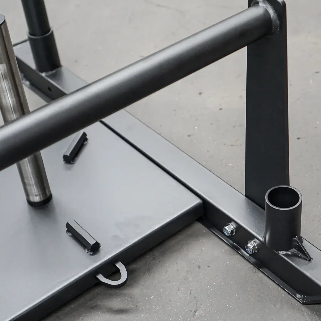 Close-up of a Power Maxx Gym Weight Sled on a gym floor, highlighting its sturdy rods and flat base. This sled has secure attachment points and is designed for strength training, providing resistance for pushing or pulling exercises.