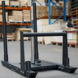 The Power Maxx Gym Weight Sled, designed for fitness training, sits on a concrete floor in a warehouse. The background displays shelves stocked with boxes and equipment, creating the perfect atmosphere for an intense workout session.