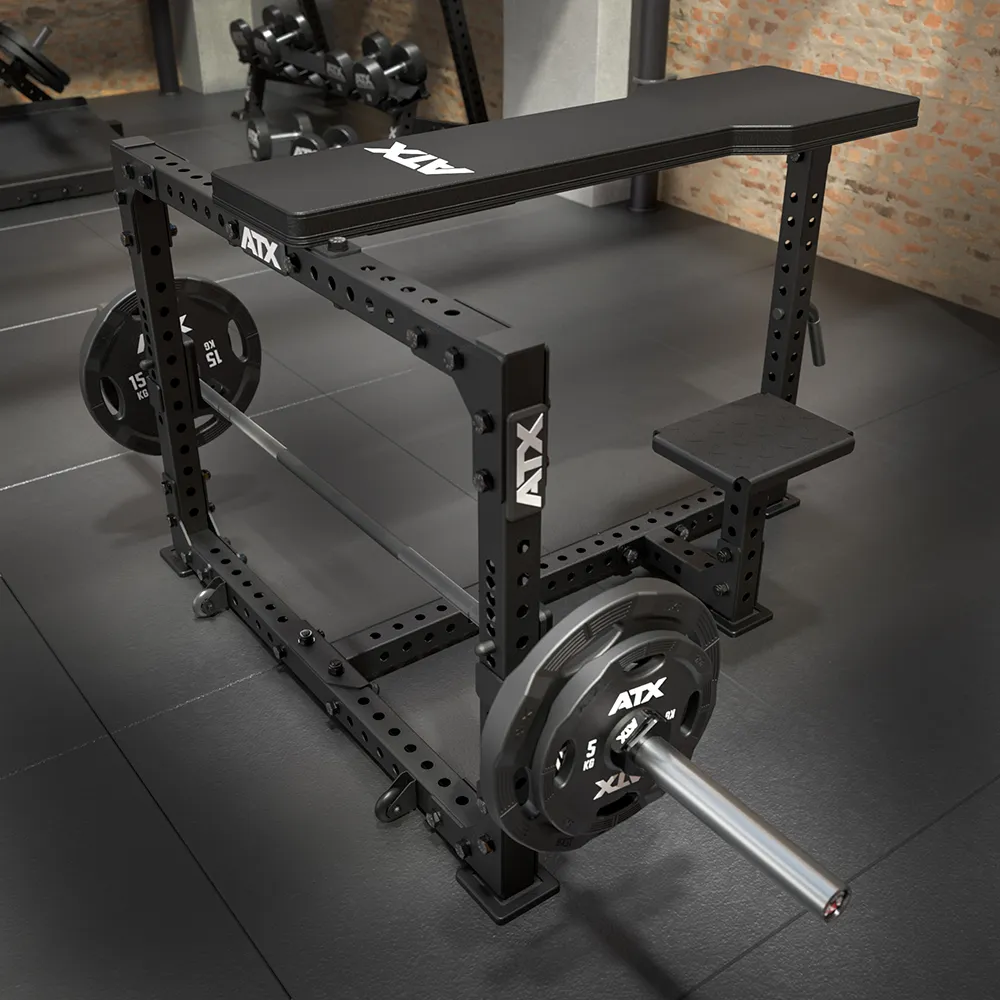 The ATX® Seal Row Bench, black and adjustable, is set on a rubber gym floor with a loaded barbell, weight plates, and dumbbells visible in the background.
