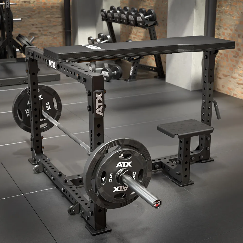 A sturdy black ATX® Seal Row Bench with a loaded barbell, weight plates, and a small step sits in a modern gym with exposed brick walls and a dumbbell rack in the background.