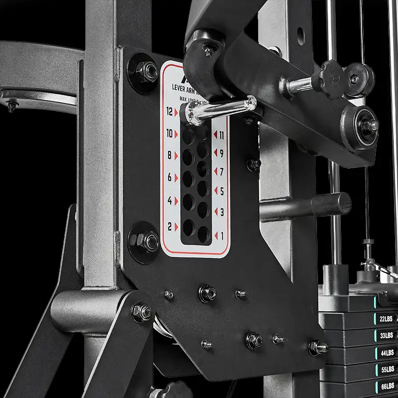 Close-up of the ATX® Triplex Weight Stack Gym's adjustment panel featuring numbered holes and a metal pin for selecting resistance; weight stack and mechanical parts are visible.
