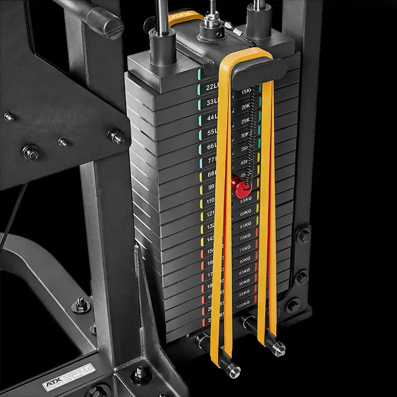 Close-up of the ATX® Triplex Weight Stack Gym shows labeled plates, colored indicators, and a red pin for weight selection. The sleek black equipment features striking yellow and orange accents.