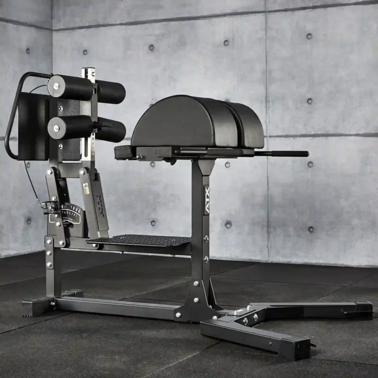 A glute-ham raise machine stands in a gym setting against a concrete wall. The equipment, ideal for glute extensions, features padded supports and adjustable settings for strength training exercises. The floor is covered with black mats for added comfort and safety.