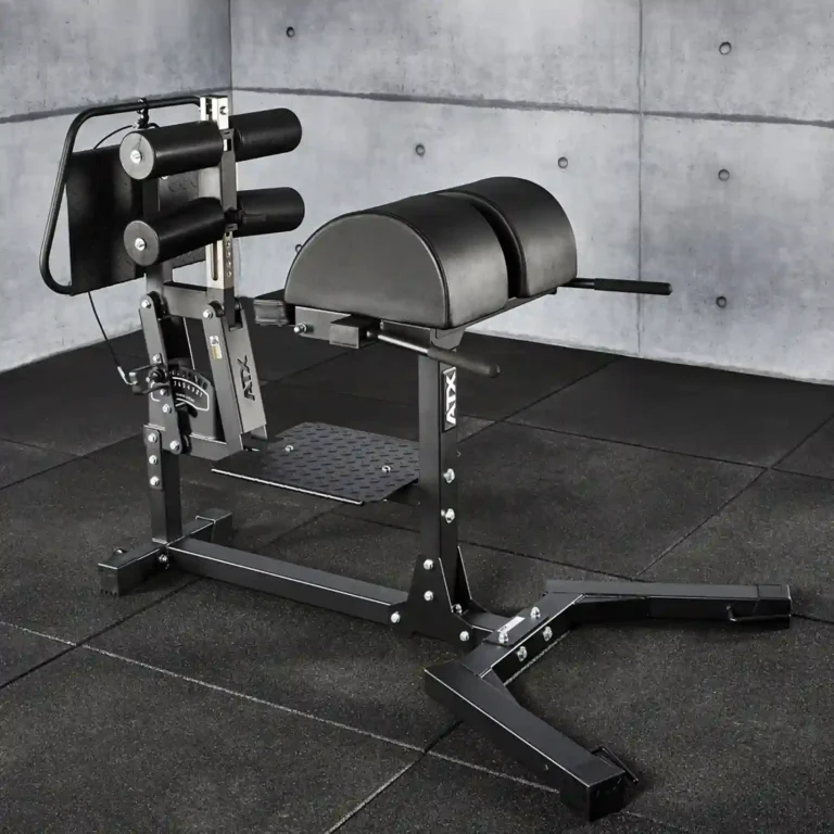 A glute and ham raise machine graces the gym space, its black padded supports set against a concrete wall. The sturdy metal frame rests securely on a rubber floor mat, blending functionality with sleek design in this modern setting.