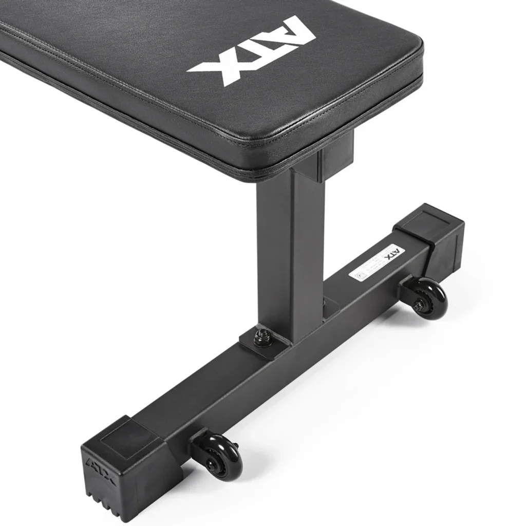 A close-up of the ATX® Flat Workout Bench Attachment shows its black padded surface with ATX branding. This durable bench features a robust metal support and two small wheels for easy mobility, making it an ideal fitness accessory.