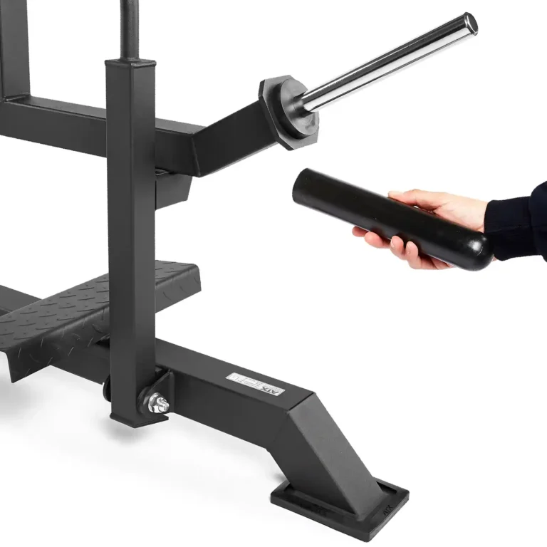 A person holds a cylindrical black object near an ATX fitness sled next to a calf raise machine. The sled features a vertical post with a peg for handles or weights, while the base includes a small platform and bolt, suggesting setup or adjustment.