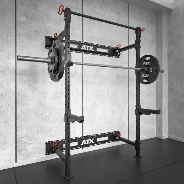 An ATX® Folding Squat Rack 500 with a loaded barbell stands in a minimalist gym, showcasing gray concrete walls and black flooring.