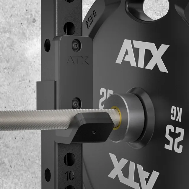 Close-up of a barbell with a 25 kg plate on the ATX® Folding Squat Rack 500, showing safety hooks and adjustment holes on the rack.