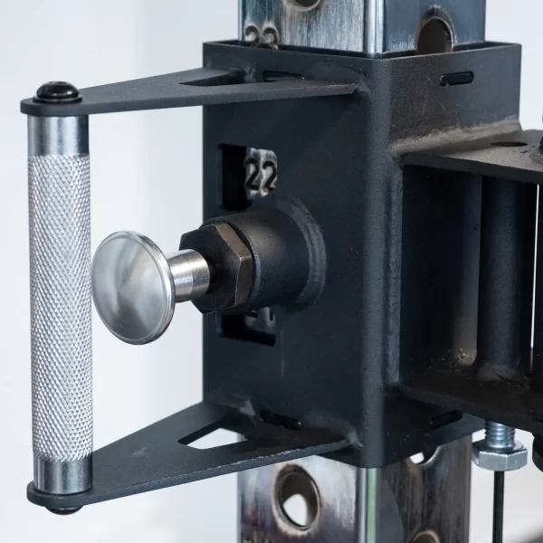 Close-up of an ATX® Power Cage with Cables featuring a black metal adjustable mechanism with a silver knob and textured handle, attached to a metallic post with holes.