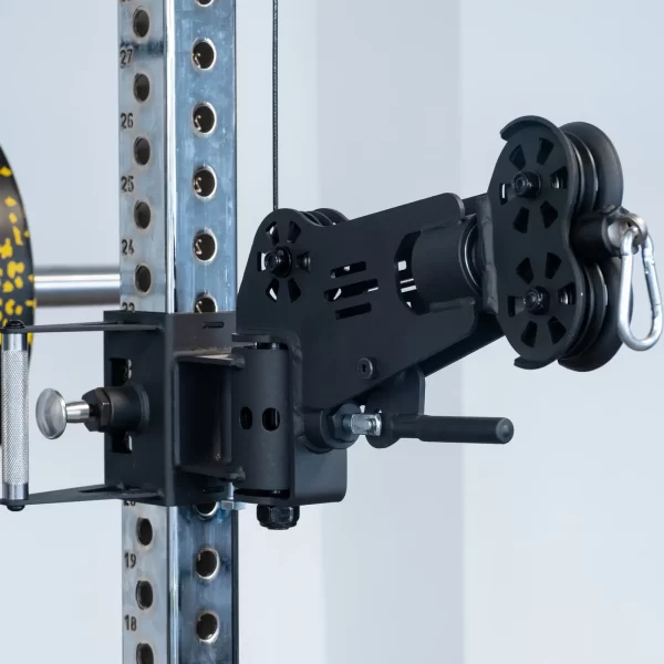 A close-up of the ATX® Power Cage with Cables attached to a metal gym rack. The setup features a black adjustable arm, pulleys, and visible screws and holes on the sturdy frame against a plain, light-colored wall backdrop.