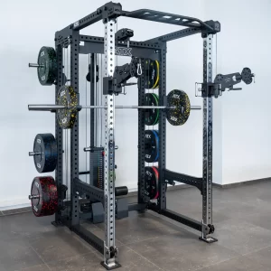 The gym features an ATX® Power Cage with Cables, equipped with various weight plates, a barbell on safety bars, and pulley attachments, all set against gray tiled floors and white walls.