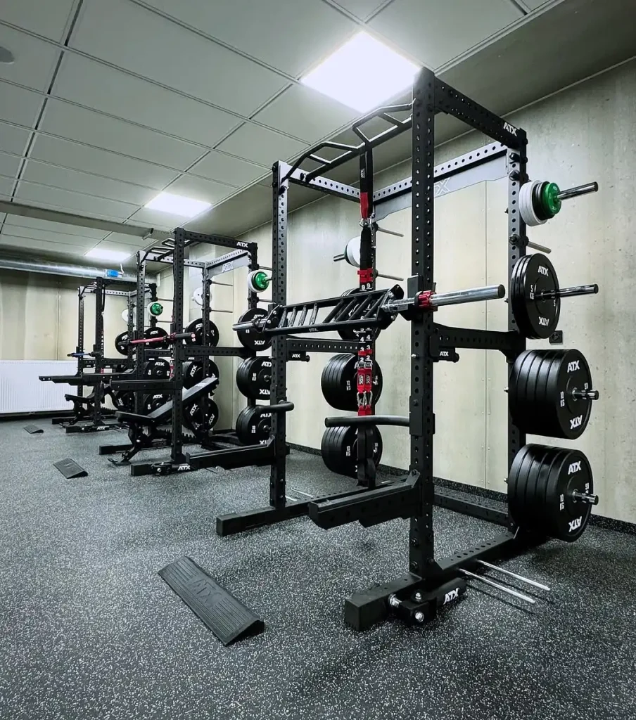 A modern gym featuring the Commercial Power Rack 780, loaded barbells, resistance bands, and strength equipment on a rubberized floor, set against concrete walls under bright ceiling lights.