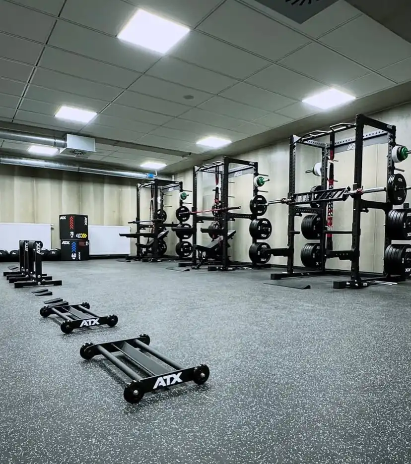 Modern gym with squat racks, the Commercial Power Rack 780, barbells, weight plates, and pull-up bars along the back wall. Black ATX parallettes rest on speckled rubber flooring. Ceiling lights brighten the clean space.