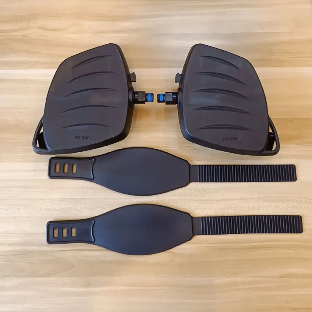 Two Spin Bike Pedal MATRIX 9/16 with textured surfaces and attached blue components are on a wooden surface, accompanied by two black adjustable straps.