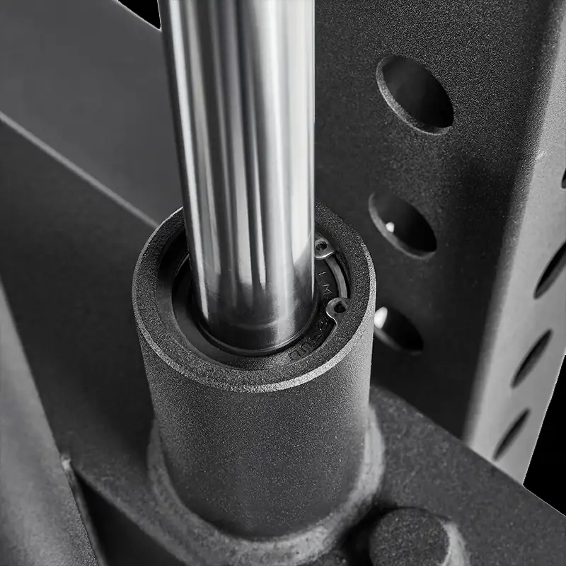 Close-up of the ATX® Vertical Leg Press’s chrome steel barbell in a black metal sleeve with bush bearing, positioned next to a perforated upright rack—components typical for this gym equipment setup.