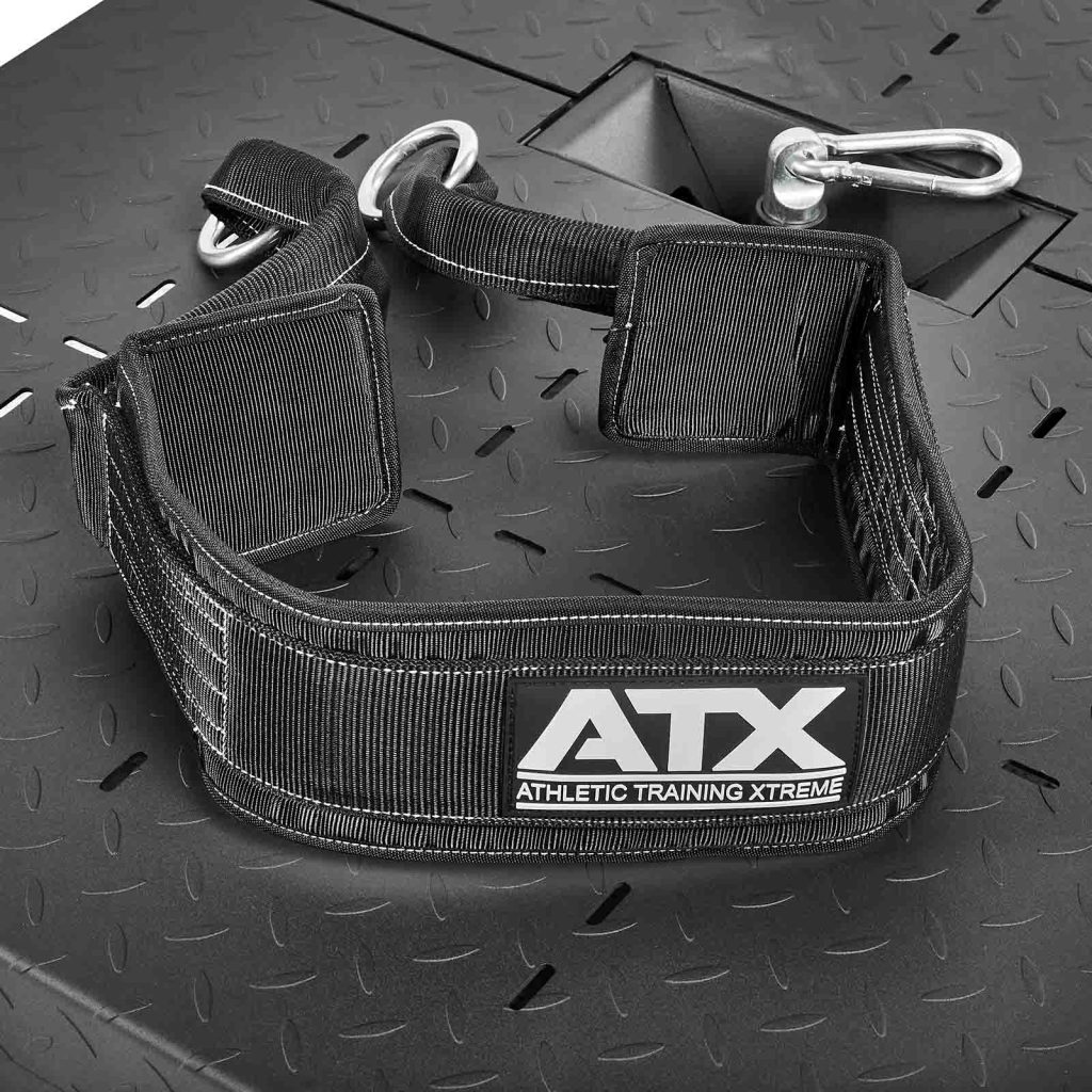 A black adjustable workout harness with a silver carabiner, labeled ATX Athletic Training Xtreme, is set on a textured metal surface with large screws and a diamond plate pattern. Designed for use with the ATX-BSM-760 Belt Squat Machine.