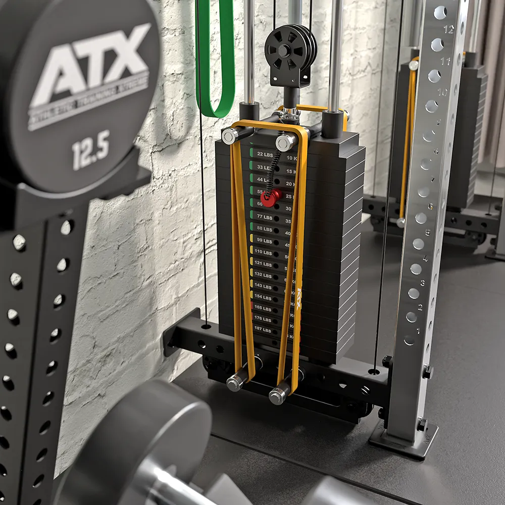 Close-up of a gym weight stack with plates, resistance bands, and a selection pin. A 12.5 kg dumbbell rests in front of the ATX Half Rack with Cable Crossover, all set against a textured white wall background.